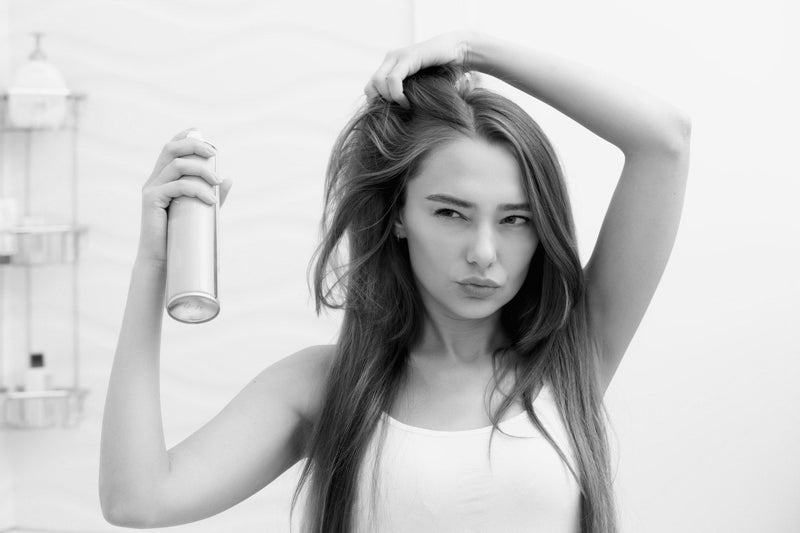 Woman spraying dry shampoo onto her roots — Kija Hair Salon